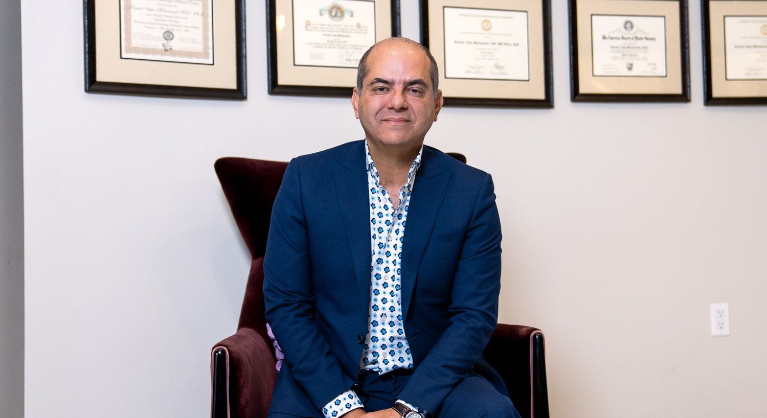 Person sitting in chair with framed certificates behind.